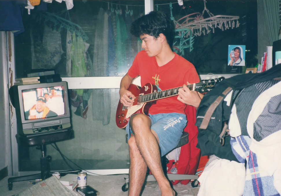 四人一部屋の狭い学生寮でギターを弾く佐藤政樹
